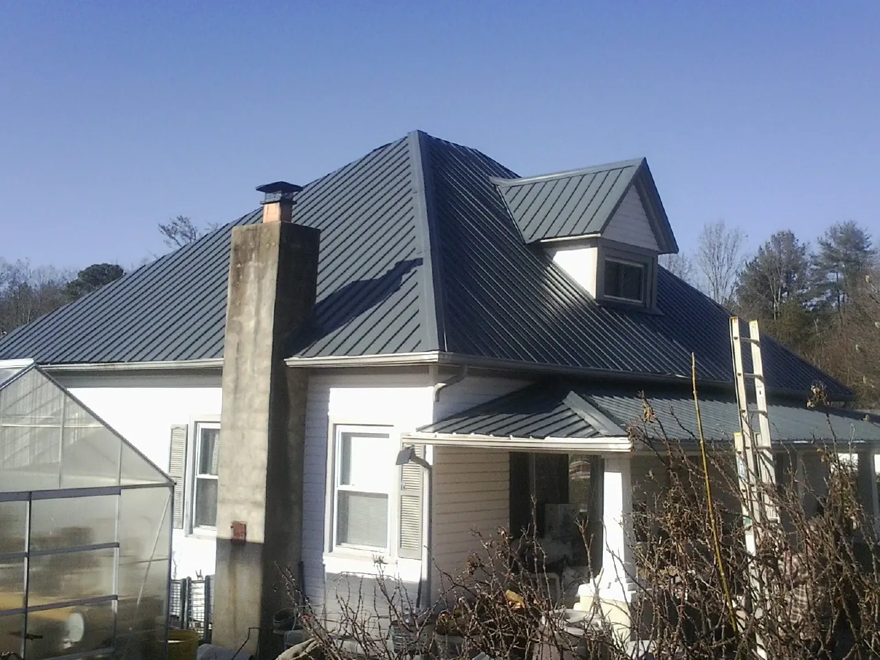 Dark blue standing seam metal roof on a white farmhouse with dormer — Slate & Tile Roof Repair by Roofing Brothers in Queens Village
