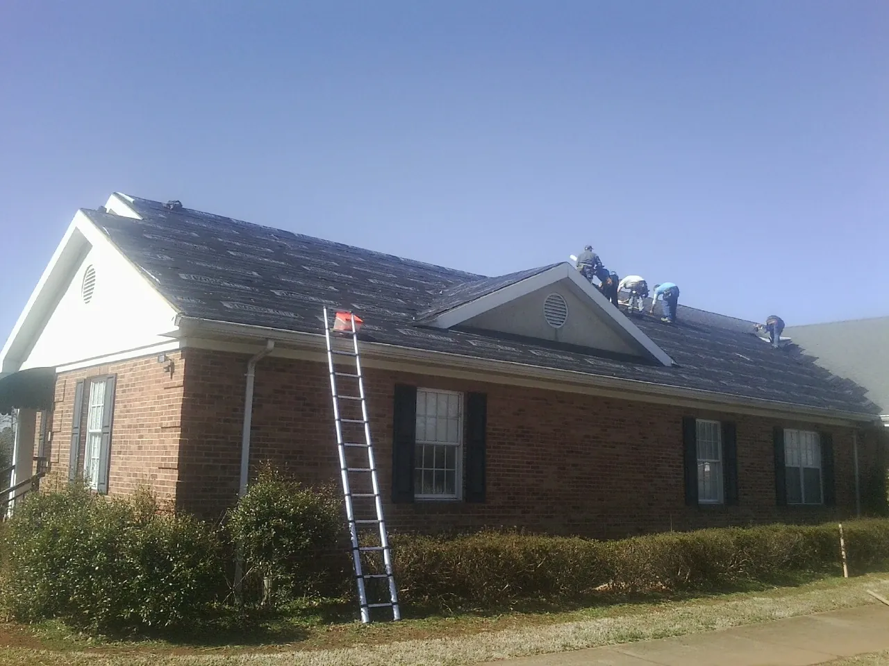 Crew tearing shingles off a brick ranch roof with a ladder set — Emergency Roof Repair work by our crew in Queens Village