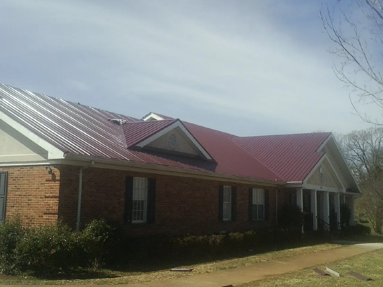 Red metal roof with gabled entries on a long brick building, from a Hail Damage Roof Repair job in Queens Village
