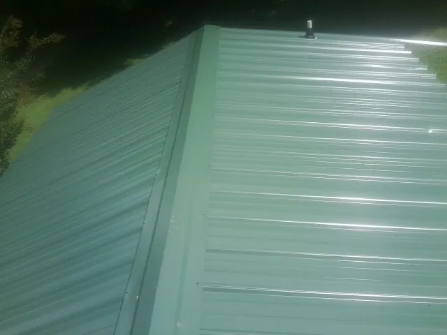 New green metal panels meeting at the ridge of a roof — Flat Roof Repair work by our crew in Queens Village