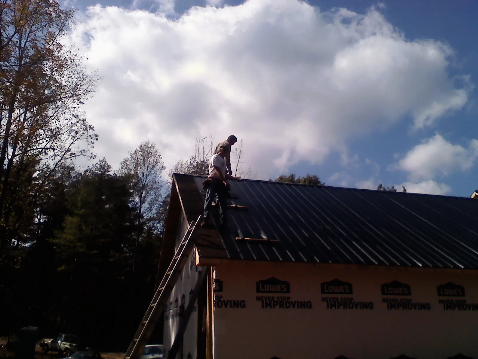 Roofer fastening dark metal panels high against a cloudy sky, from a Roof Inspection job in Queens Village