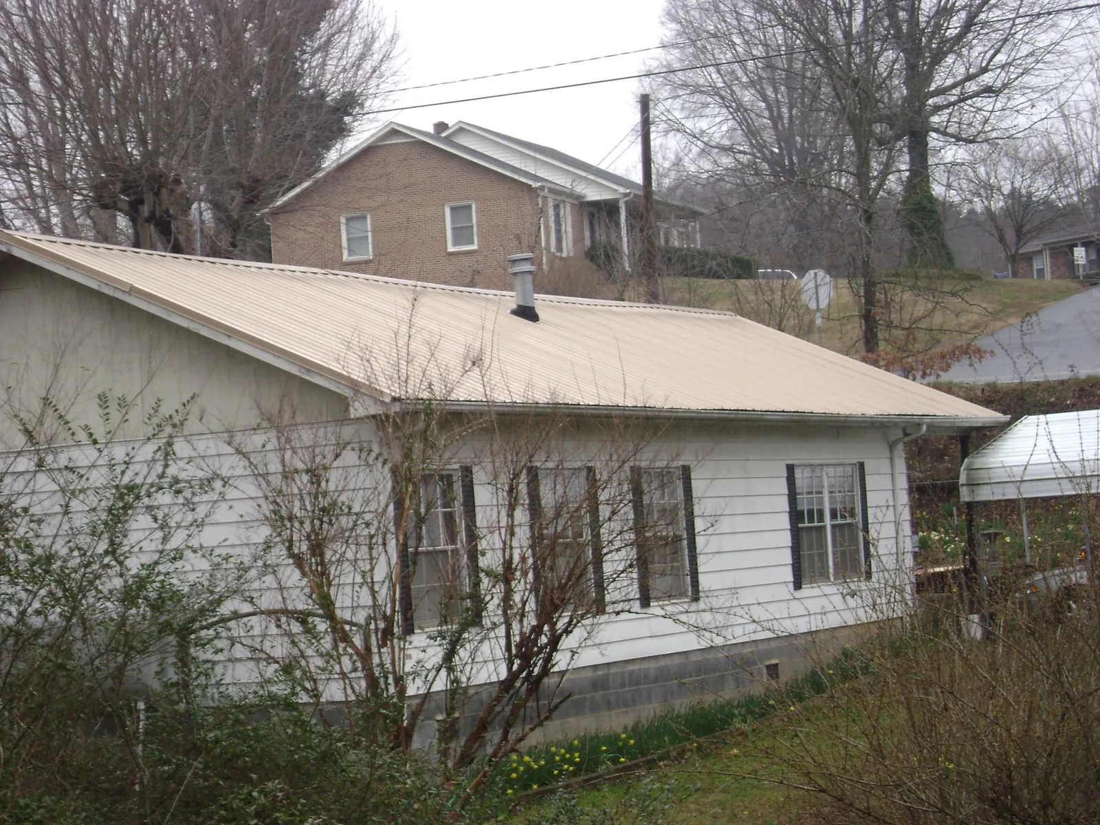 Tan metal roof on a white sided house set into a hillside — Commercial Roofing by Roofing Brothers in Queens Village