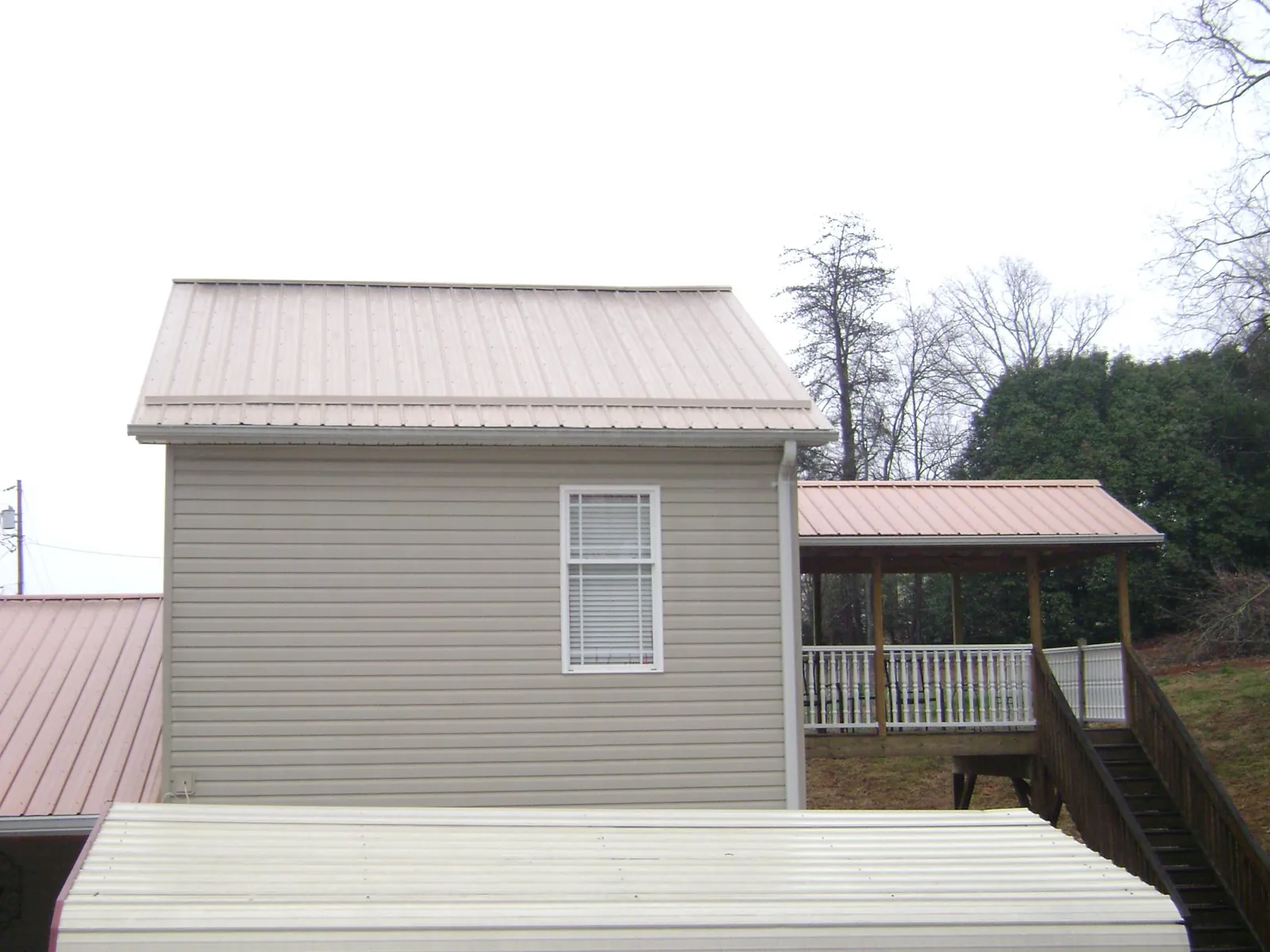 Tan metal roofs on a two story addition and attached porch, from a Roof Replacement job in Queens Village